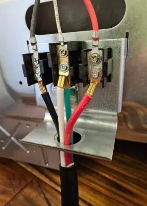 Close-up of black, red and white conductors with a green ground landed on the terminal block of an appliance, with a strain relief below